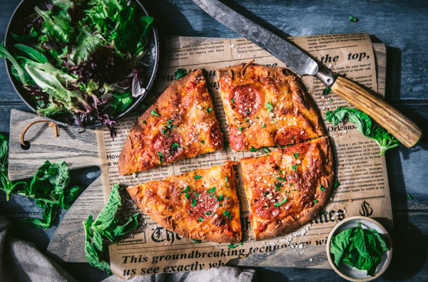 Horizontal shot of a wooden cutting board with a sliced flatbread pizza