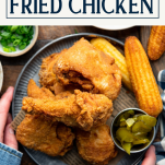 Overhead shot of hands serving a platter of the best fried chicken recipe with text title box at top