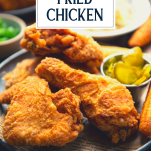 Close up side shot of a plate of the best fried chicken recipe with a side of pickles and text title overlay