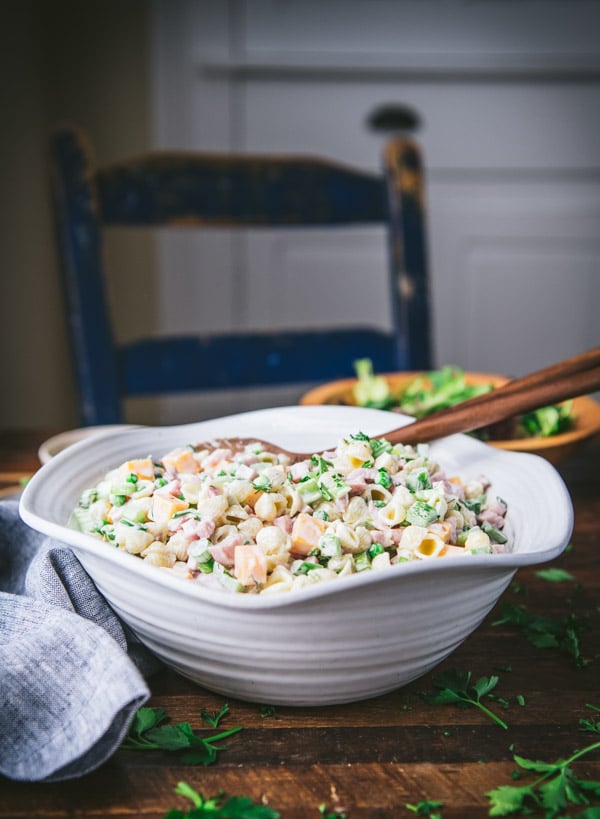 Side shot of ham pasta salad in a white bowl on a wooden table.