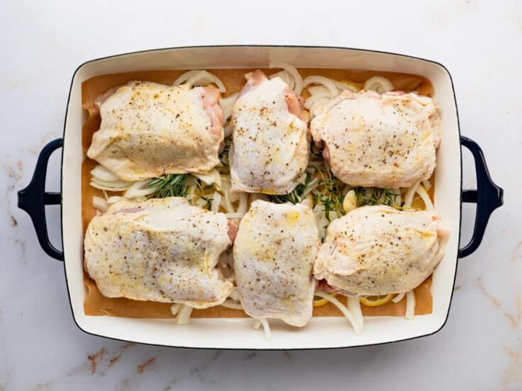 Arranging chicken thighs on top of lemons, onions, and herbs.