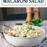 Side shot of a bowl of macaroni salad on a table with text title box at top
