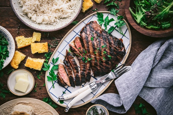 Horizontal shot of a marinated flank steak served on a wooden table with a side of rice and salad