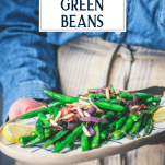 Side shot of hands holding a tray of oven roasted green beans with text title overlay