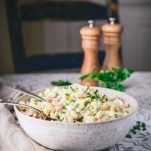 Side shot of a big bowl of old fashioned macaroni salad on a dinner table with salt and pepper shakers in the background