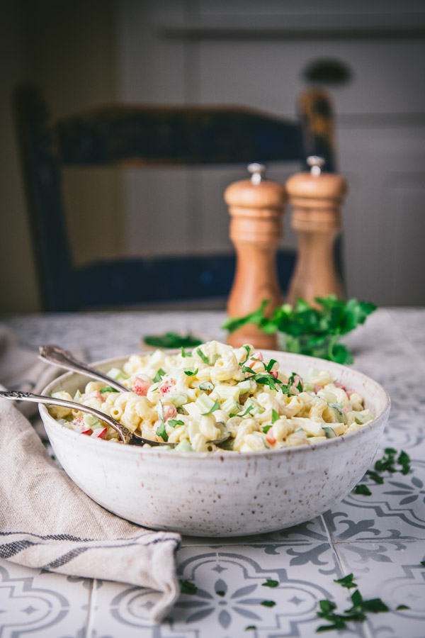 Side shot of a big bowl of old fashioned macaroni salad on a dinner table with salt and pepper shakers in the background