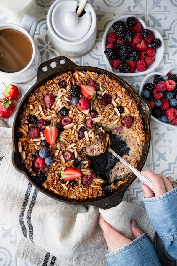Hands serving baked oatmeal with almonds and berries on a breakfast table