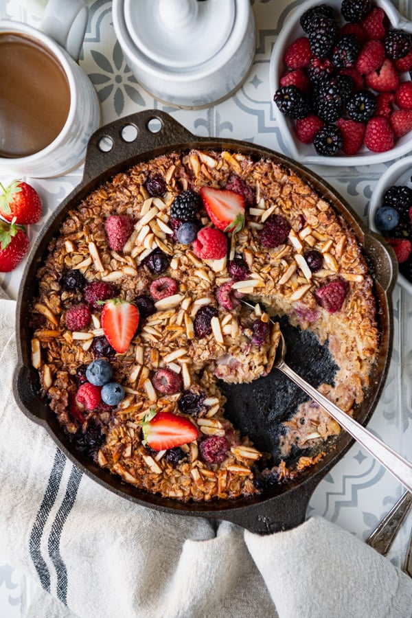 Spoon in a pan of the best baked oatmeal recipe served with fresh strawberries raspberries blueberries and blackberries