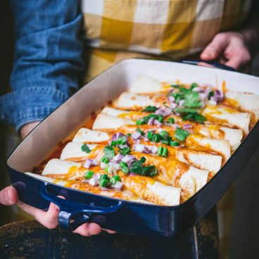 Square front shot of hands holding a pan of beef enchiladas