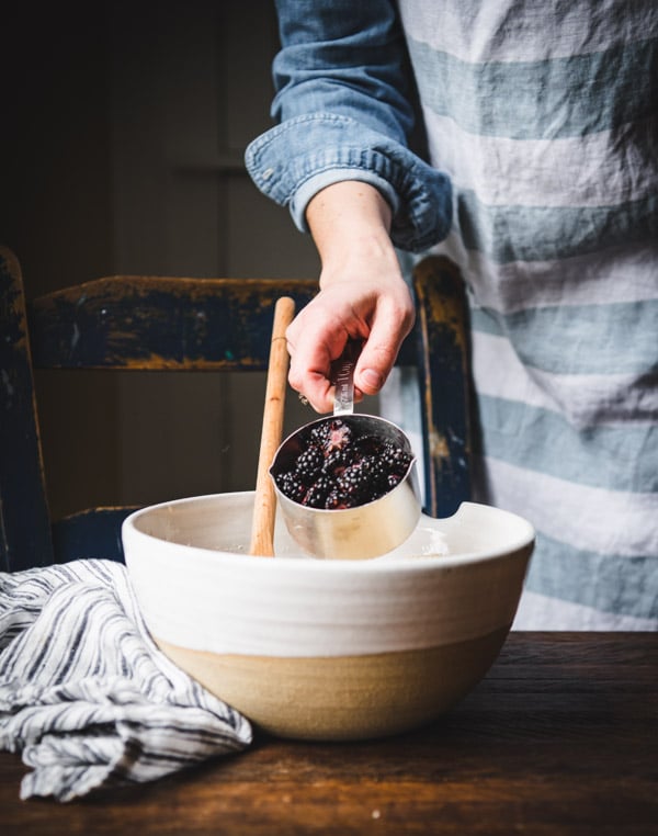 Adding fresh blackberries to a large mixing bowl