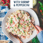 Hands tossing a bowl of chicken pasta salad with wooden servers and text title overlay at top