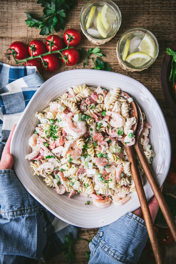 Hands holding a bowl of creamy chicken pasta salad with mayo