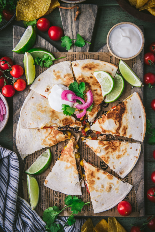 Overhead shot of a wooden cutting board with a sliced chicken quesadilla and toppings.