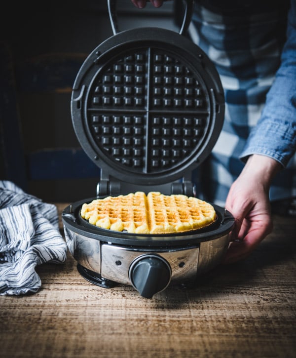 Process shot showing how to make cornbread waffles in a waffle iron.