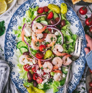 Hands holding a platter of a Greek salad with shrimp