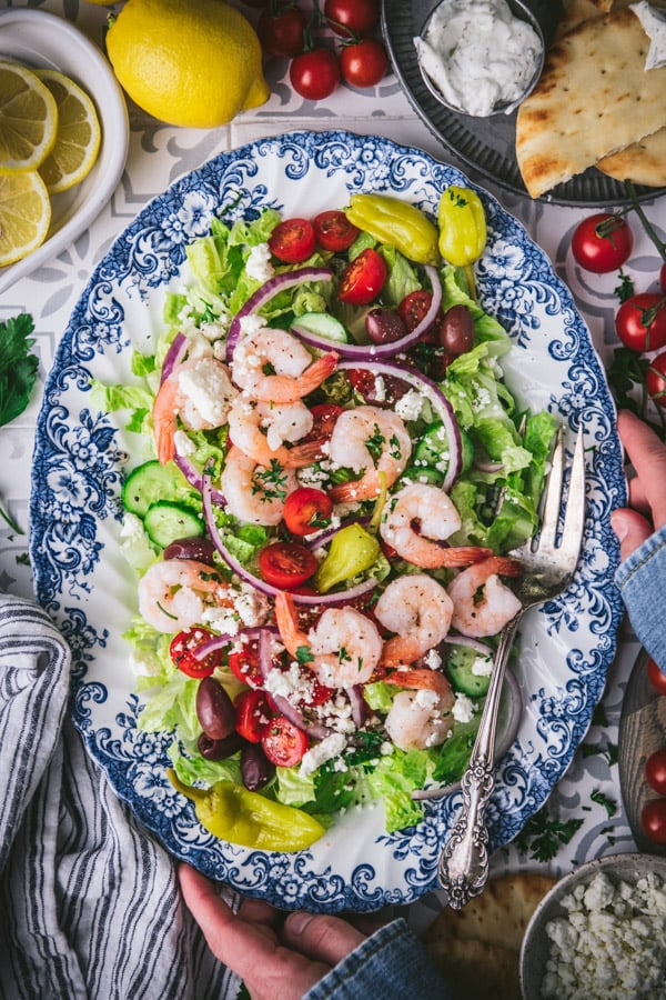 Hands holding a platter of a Greek salad with shrimp