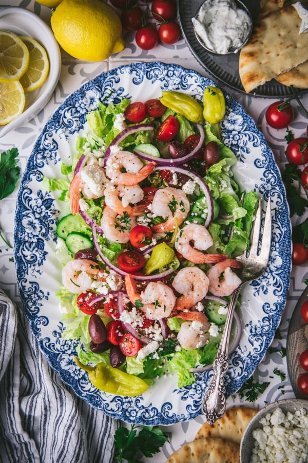 Overhead shot of greek salad with shrimp on a table with pita bread