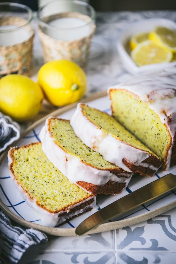 Sliced lemon loaf cake on a ceramic platter with a gold knife