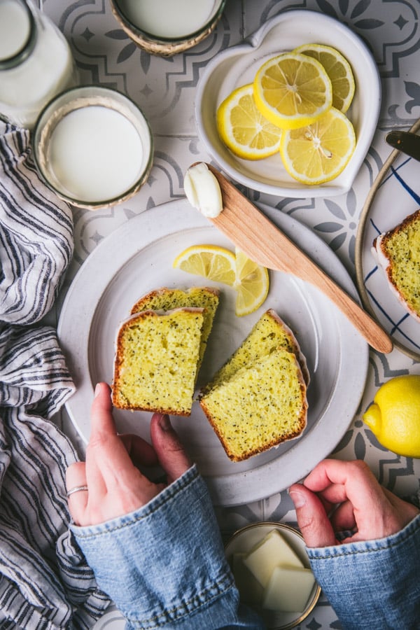 Hands picking up a slice of lemon loaf cake from a white plate