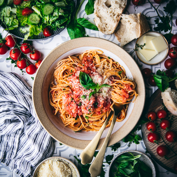 Square overhead image of a table with pomodoro sauce and spaghetti, salad, and bread.