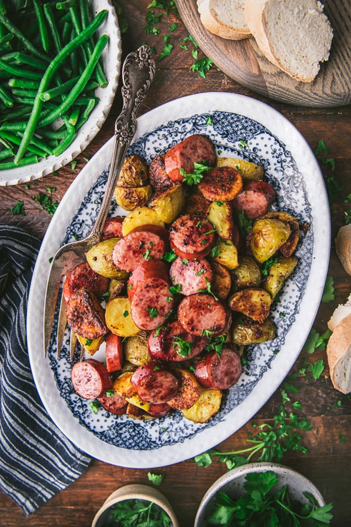 Tray of sheet pan smoked sausage and potatoes on a wooden dinner table.