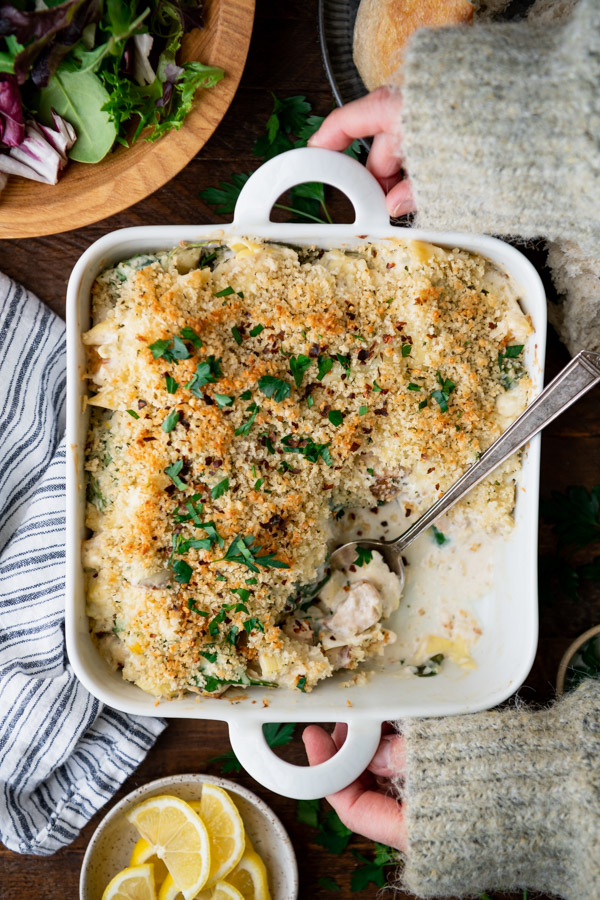 Overhead shot of hands holding a spinach artichoke chicken casserole on a wooden table