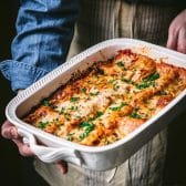 Square shot of hands holding a dish of the best spinach lasagna recipe.