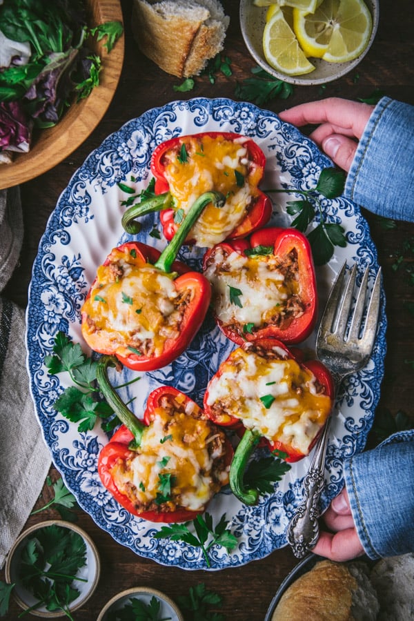 Hands holding a plate of stuffed bell peppers with rice and ground beef