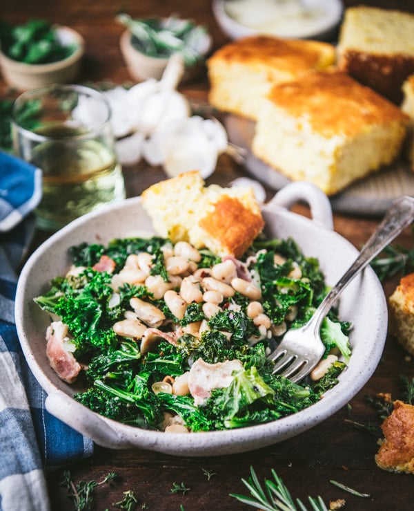 Close up side shot of a fork in a bowl of beans and greens with cornbread.