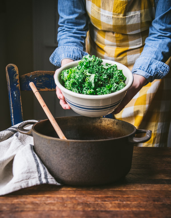 Adding kale to a Dutch oven.