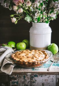Side shot of the best apple pie recipe sitting on a wooden chest with flowers in the background