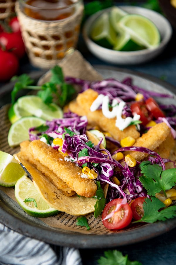 Close up side shot of easy fish tacos with slaw on a plate with fresh herbs and lime wedges