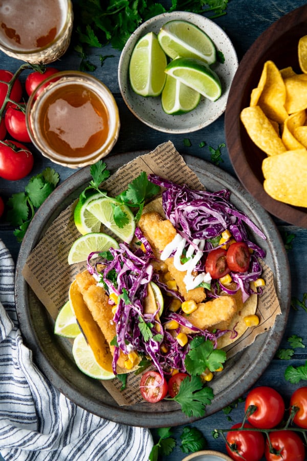 Overhead shot of a table with chips, limes, beer, and easy fish tacos on a plate