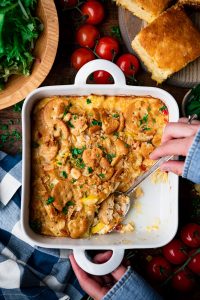 Overhead shot of hands serving southern squash casserole from a white dish