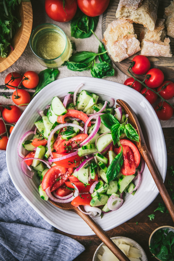 Wooden spoons in a white bowl full of the best cucumber onion tomato salad recipe