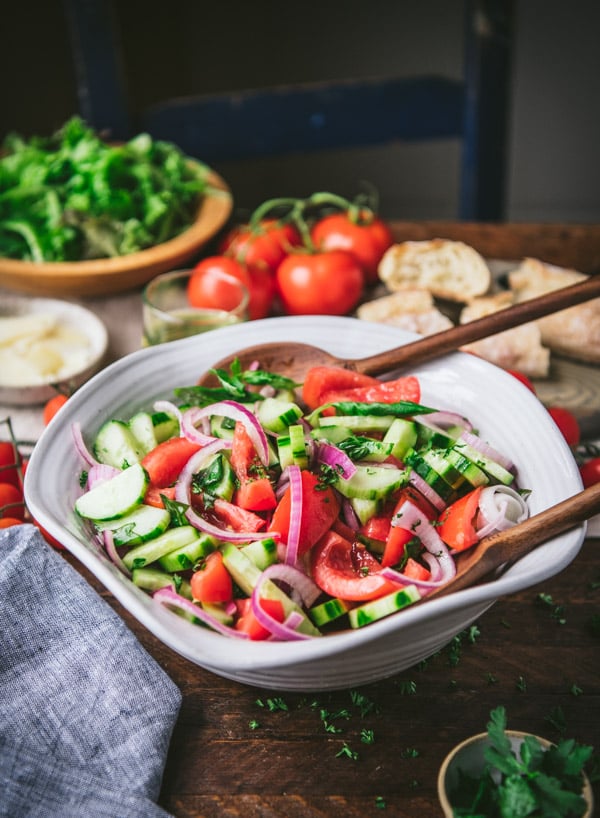 Side shot of a bowl of cucumber tomato onion salad on a wooden table