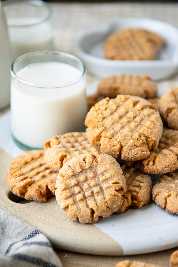 Close up side shot of a glass of milk with a pile of 3 ingredient peanut butter cookies
