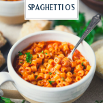 Side shot of a spoon in a bowl of homemade spaghettios with text title overlay