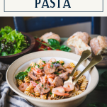 Side shot of a bowl of shrimp and sausage pasta on a table with text title box at top