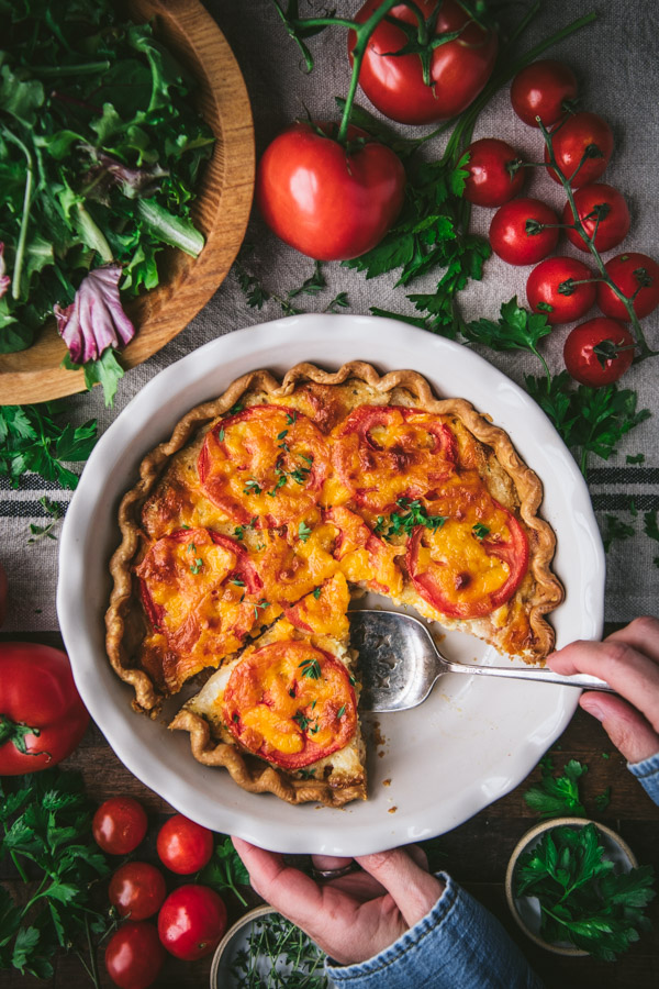 Overhead shot of hands serving a southern tomato pie from a white dish