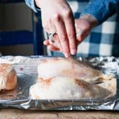 Sprinkling bbq dry rub on bone-in skin-on chicken breasts.