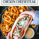 Overhead image of hands holding a chicken cheesesteak on a plate with text title box at top