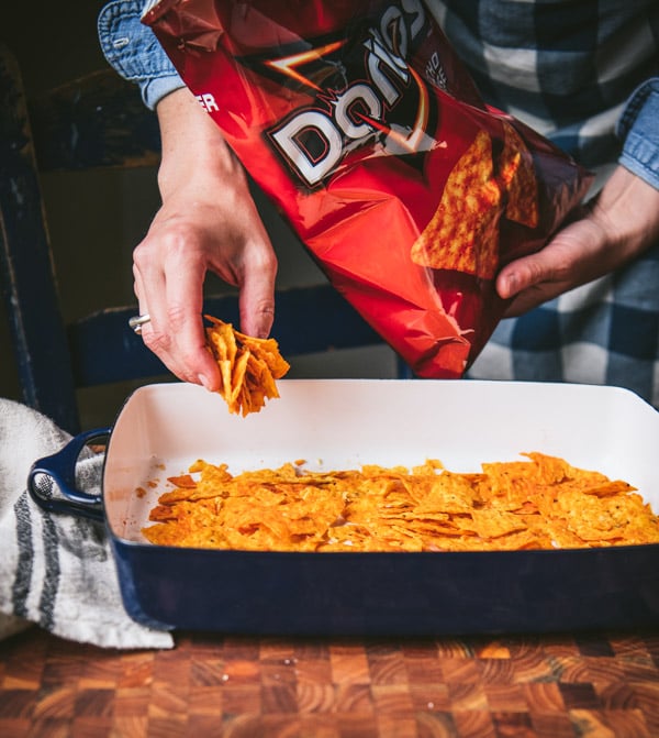 Arranging crushed Dorito chips in a baking dish