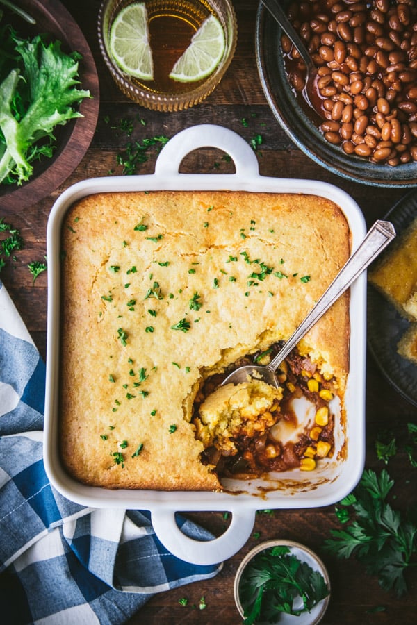 Spoon in a dish of leftover pulled pork casserole with cornbread topping on a wooden table