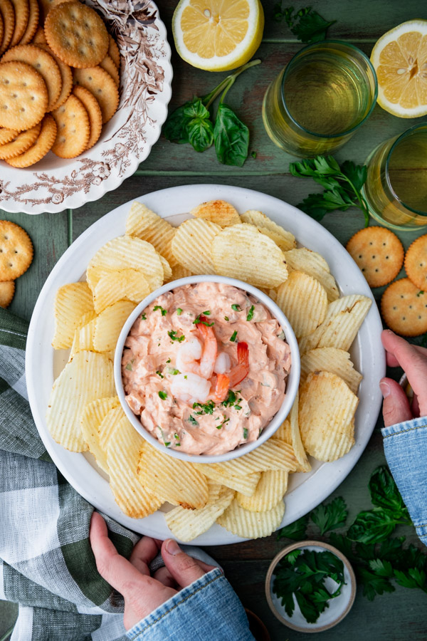 Hands holding a white plate with potato chips and cream cheese shrimp dip