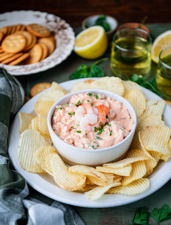 Side shot of shrimp dip with chips and crackers on a table with wine