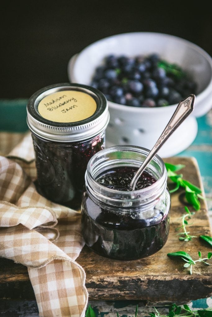 Two jars of blueberry jam on a wooden board