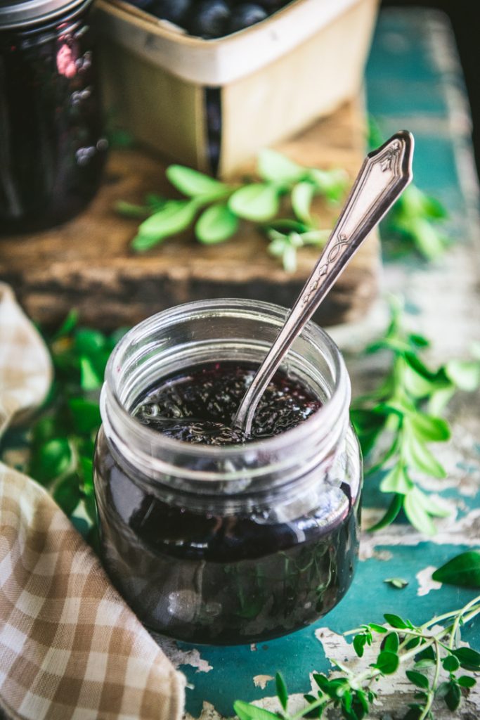An easy blueberry jam recipe on an antique table with a spoon in the jar