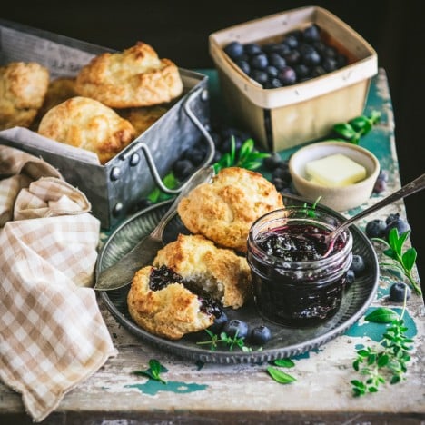 Square shot of homemade blueberry jam on a table with biscuits