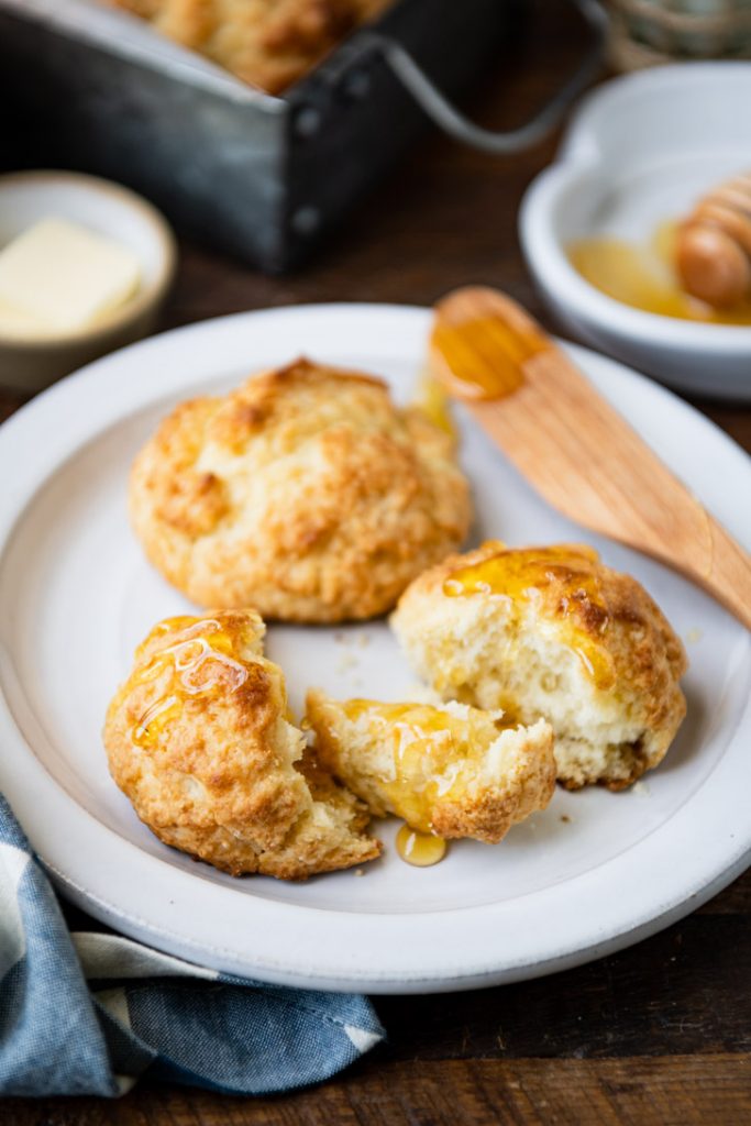 Two drop biscuits on a white plate with honey